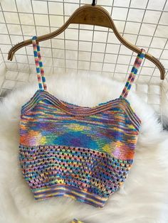 a multicolored crocheted crop top hanging on a hanger next to a white fur rug