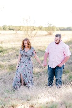 a man and woman holding hands walking through tall grass