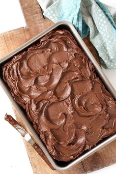 a pan filled with chocolate frosting sitting on top of a wooden table next to a napkin