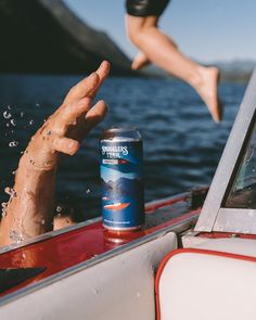 a person jumping into the air from a boat with a can of beer in front of them