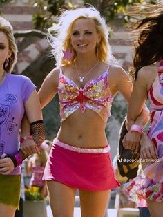 three women in pink and purple outfits walking down the street with one holding a cell phone