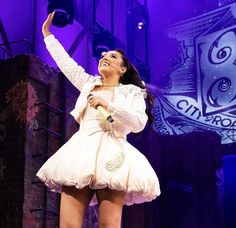 a woman standing on top of a stage with her arms in the air while wearing a white dress