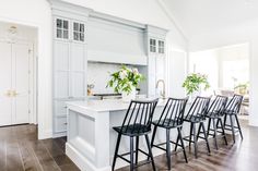 a kitchen with white cabinets and black barstools in the center island, surrounded by wooden flooring