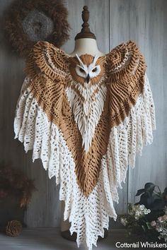 an owl shawl is hanging on a mannequin headdress with flowers in the background