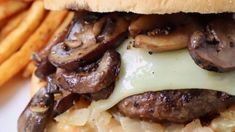 a cheeseburger with mushrooms and onions on it is next to french fries in the foreground