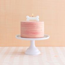 a pink cake on a white pedestal with a lit candle in the middle and a small dog head on top