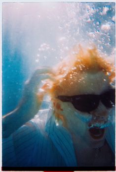 a man wearing sunglasses under water with his hair in the air and sun shining on him