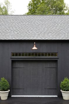 two potted plants in front of a black garage with a copper bell on top