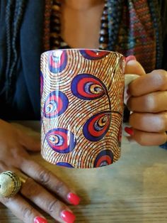 a woman sitting at a table with a coffee cup in front of her, holding the mug