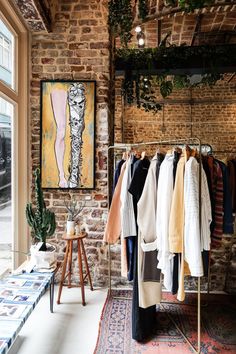 a clothing rack in front of a brick wall with clothes on hangers and a painting