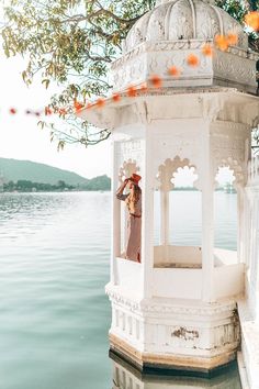 a woman is standing in a white gazebo on the water's edge with orange flowers around her