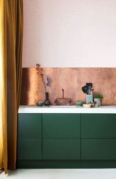 a kitchen with green cabinets and white counter tops in front of a pink brick wall