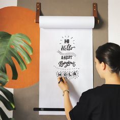 a woman is drawing on a white paper with black marker and some plants in the background