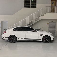 a white car parked in a garage next to a stair case and some stairs on the wall