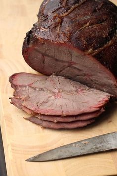 a large piece of meat sitting on top of a cutting board next to a knife