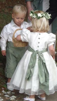 two young children dressed in white and green outfits, one is holding a wicker basket