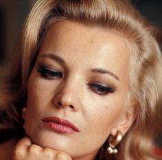 a woman with blonde hair and black eyeliners is looking at the camera while wearing gold earrings