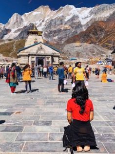 a woman sitting on the ground in front of a mountain with snow capped mountains behind her