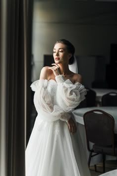 a woman standing in front of a mirror wearing a wedding dress with ruffled sleeves