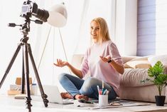 a woman sitting on the floor in front of a camera and laptop with her hands out