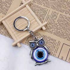 an owl keychain with blue eyes on top of a table next to a book