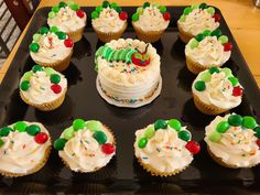 cupcakes with white frosting and candy decorations on a black tray in front of a wooden table