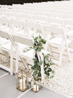 two white chairs with greenery tied to them and some candles on the ground in front of them