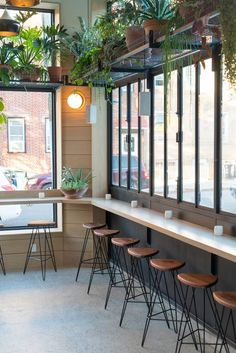 the inside of a restaurant with lots of plants on the windows and barstools