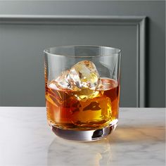 a glass filled with liquid and ice on top of a white marble counter next to a gray wall