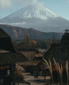 two people are walking down a path in front of a mountain with thatched roofs