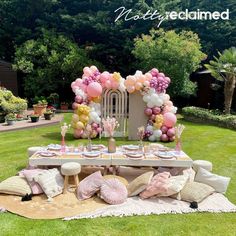 a table set up for a party with balloons and other decorations on the grass in front of it