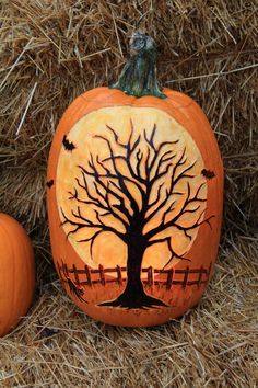 two pumpkins sitting on top of hay with a tree painted on the front and side