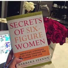 the book secrets of six figure women by barbara stanny is held up in front of a laptop