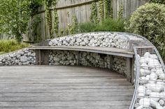 there is a bench made out of rocks on the side of a wooden deck in front of a fence