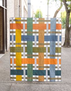 a colorful quilt on the sidewalk in front of a building