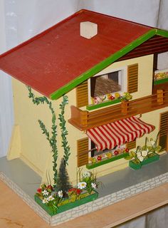 a doll house with a red roof and green shutters on the window sill