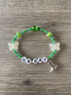 a green beaded bracelet with the word urgay on it and a butterfly charm