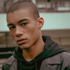 a young man wearing a black hoodie looking at the camera while standing in front of a building