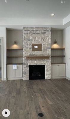 an empty living room with stone fireplace and built in shelves