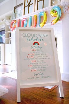 a white sign sitting on top of a wooden floor in front of a shelf filled with balloons