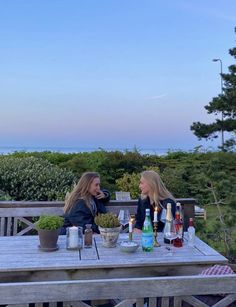 two women sitting at a picnic table with bottles of wine and candles in front of them