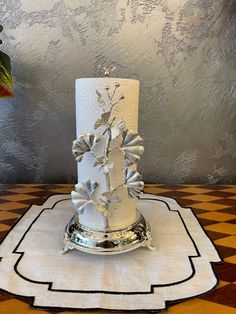 a three tiered white wedding cake with silver flowers on the top and bottom, sitting on a checkered tablecloth