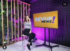 a woman is sitting on a stool in front of a tv screen with the news logo