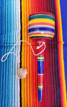 a colorful striped table cloth with a small wooden object on it's side and a string attached to the top