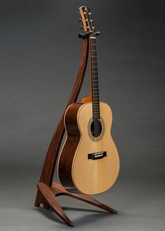 an acoustic guitar stands upright on a gray background with a wooden stand holding the guitar