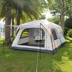 a tent is set up on the grass in front of some trees and palm trees