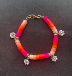 an orange and pink beaded bracelet with white flowers on it, sitting on a black surface