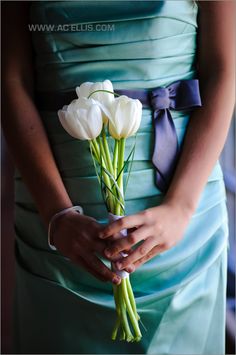 a woman in a blue dress holding a bouquet of white tulips on her wedding day