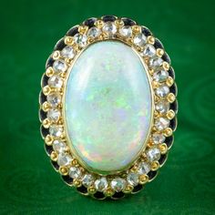 Built around a breath-taking natural opal, this remarkable mid-Century cocktail ring is sure to turn heads. The opal cabochon weighs an impressive 14 carats (approx.) and exhibits an enchanting rainbow of vibrant colours that are complemented by a halo of twinkling rose cut diamonds around the border (approx. 1.3ct total).  Opal is the birthstone of October. Their magic has been revered throughout history, desired for their enchanting rainbow of vibrant colours that shimmer and intensify with th White Ethiopian Opal Ring For Formal Occasions, Formal White Ethiopian Opal Ring, Elegant Collectible Opal Ring, Formal Ethiopian Opal Cabochon Ring, White Oval Victorian Opal Ring, Victorian White Oval Opal Ring, Victorian Style Opal Ring For Formal Occasions, Vintage Cocktail Ring, Diamond Cocktail Ring