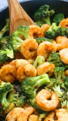 broccoli and shrimp are being cooked in a skillet with a wooden spoon